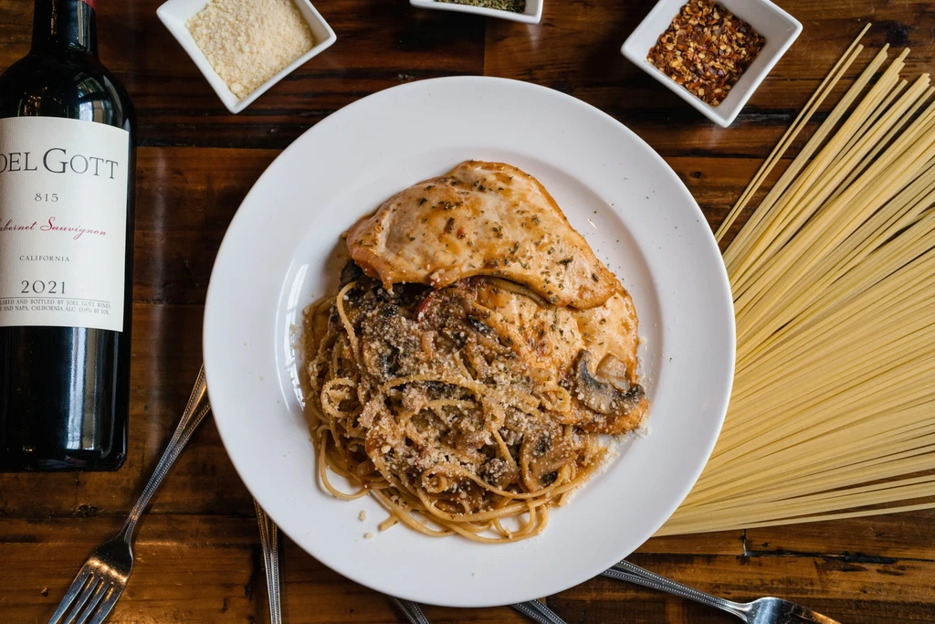 Overhead: Plated chicken pasta, wine, spices, and dry spaghetti.