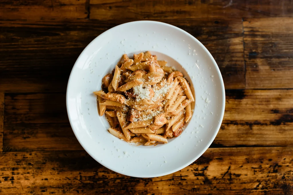 Creamy penne pasta with grated cheese in a white bowl on wood.