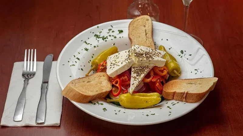 A plate of salad with feta, peppers, and bread slices on a table.