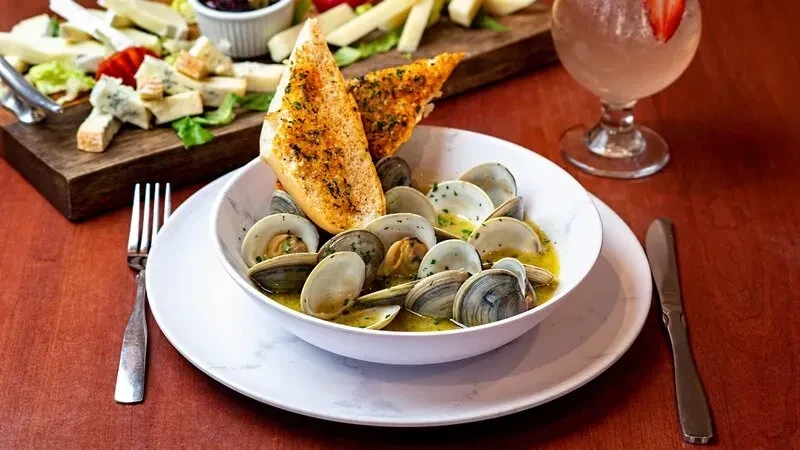 A white bowl of clams in broth with garlic bread.