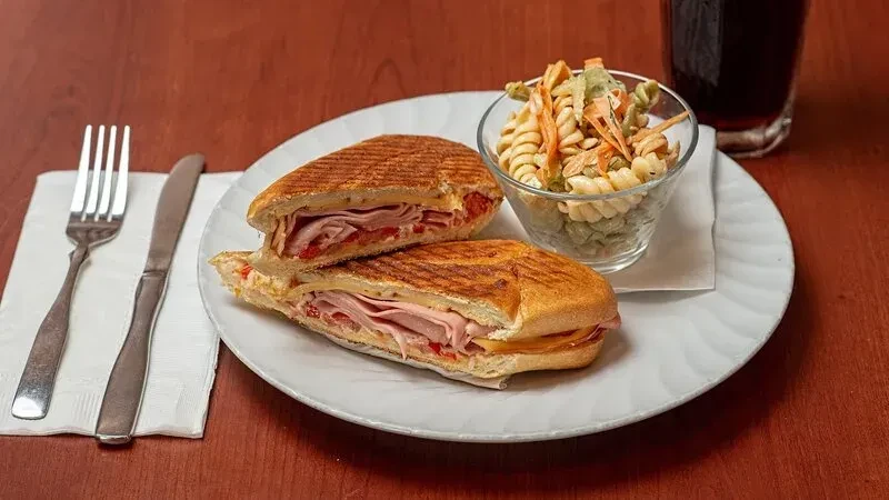 Grilled panini, pasta salad, and a beverage on a wooden table.