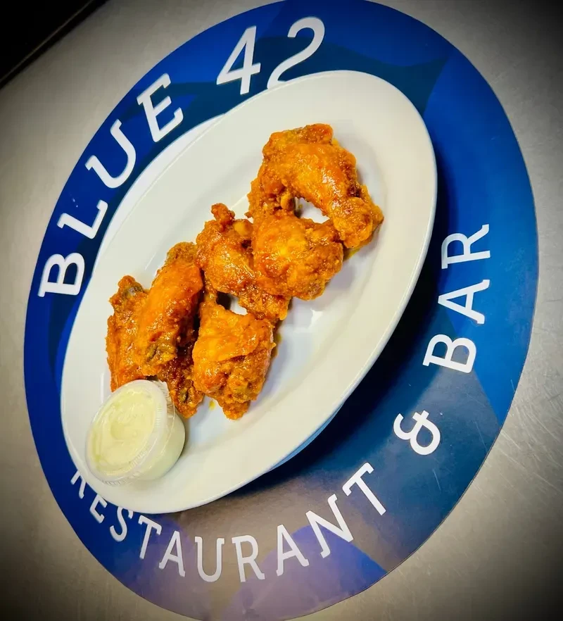 Orange chicken wings with white dipping sauce on Blue 42 mat.