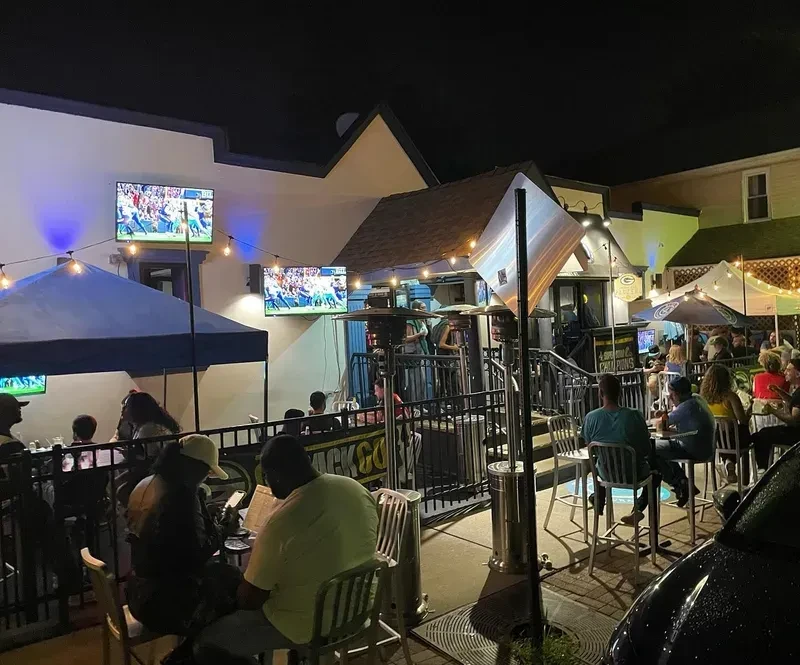 A lively outdoor bar patio at night with TVs showing sports.