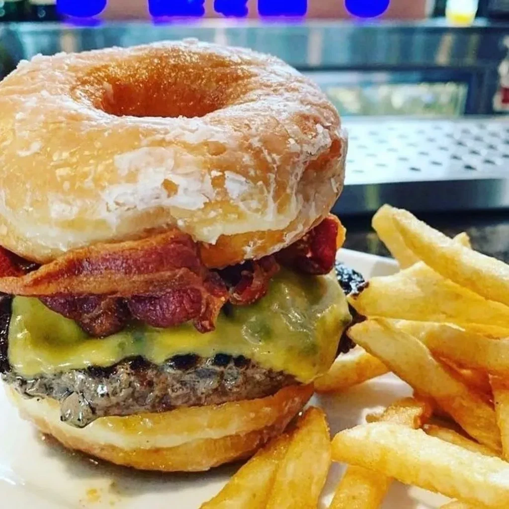 Donut burger with cheese, bacon, and a side of french fries.