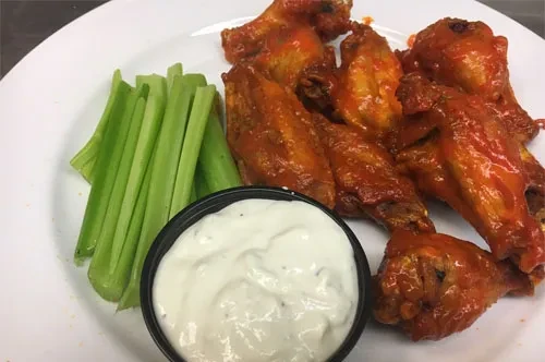 Plate of buffalo wings, celery sticks, and a side of ranch dressing.