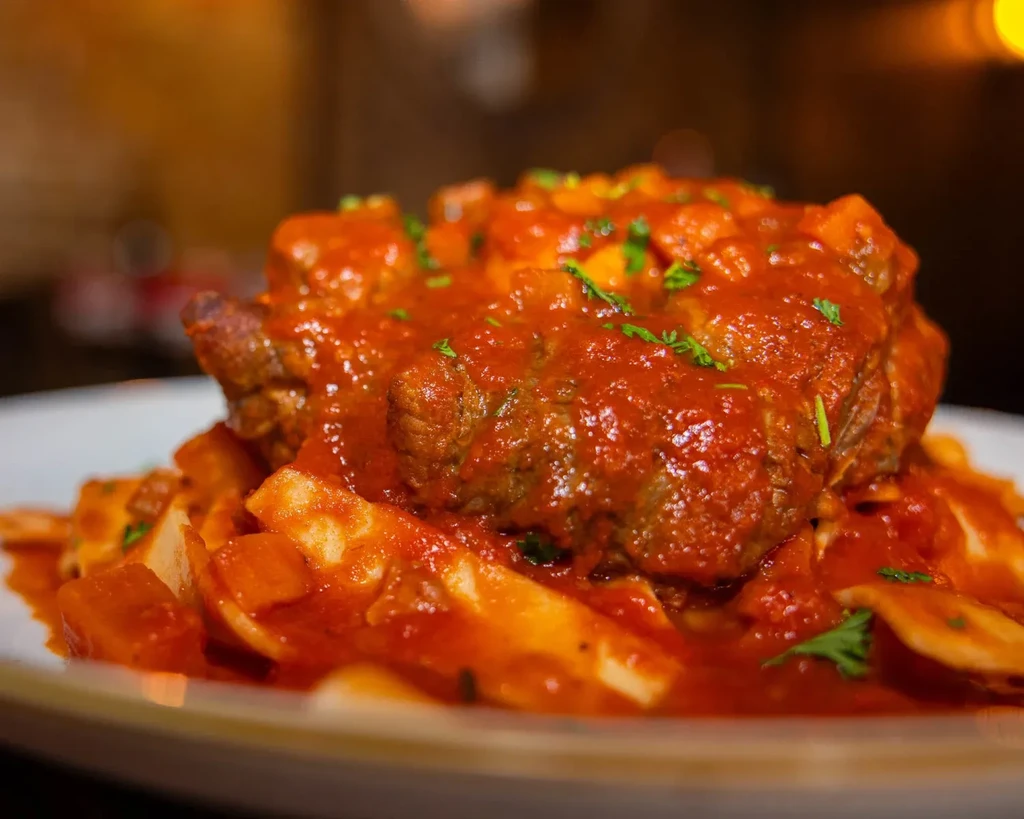 Braised meat in red tomato sauce with pasta, garnished with herbs.