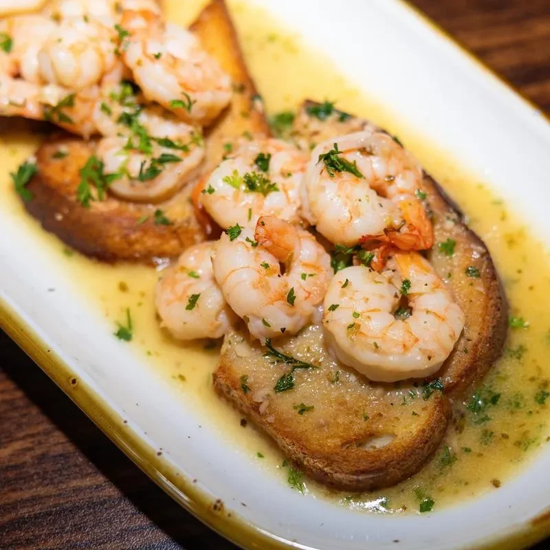 Shrimp and toast points in a lemon garlic sauce on a white plate.