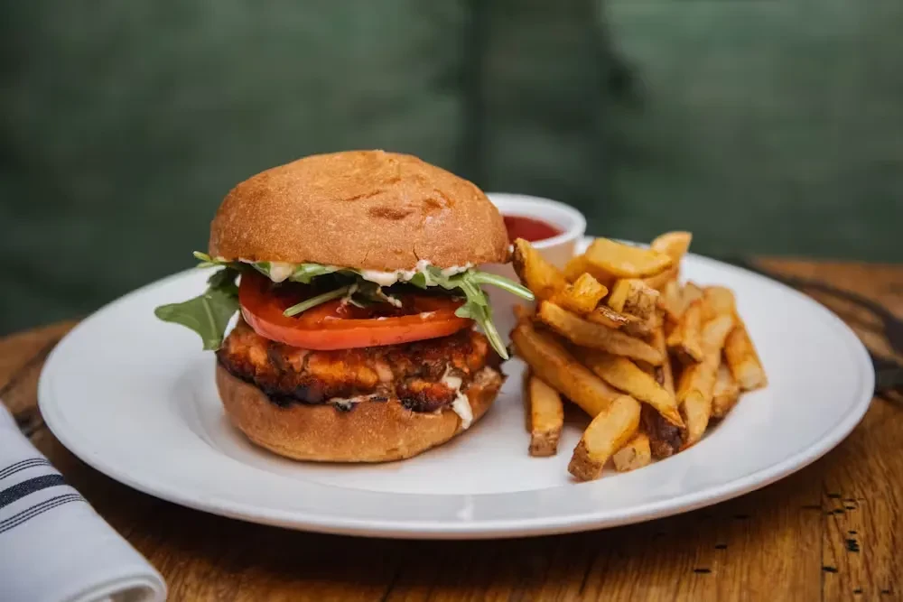 A salmon burger with tomato, arugula, and fries on a white plate.