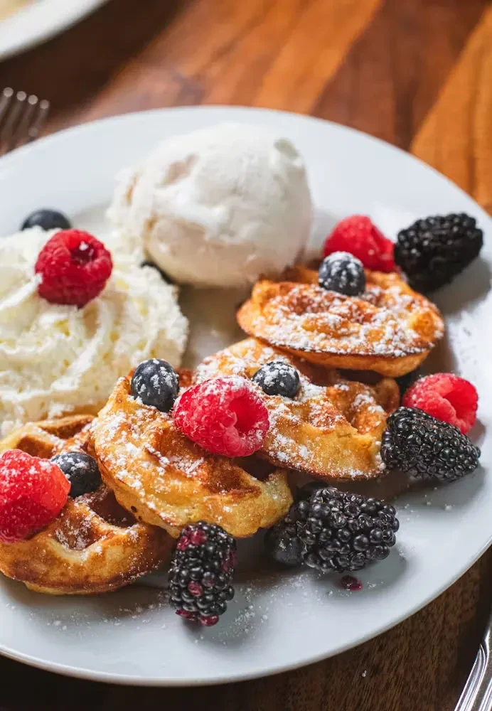 Waffles with berries, ice cream, and whipped cream on a white plate.
