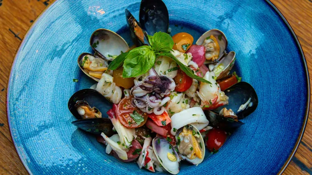 A blue bowl filled with seafood salad, cherry tomatoes, and basil.