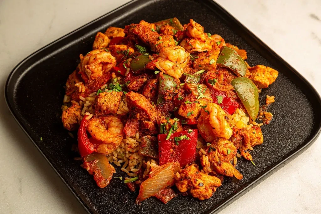Jambalaya with shrimp, chicken, sausage, and vegetables on a black plate.