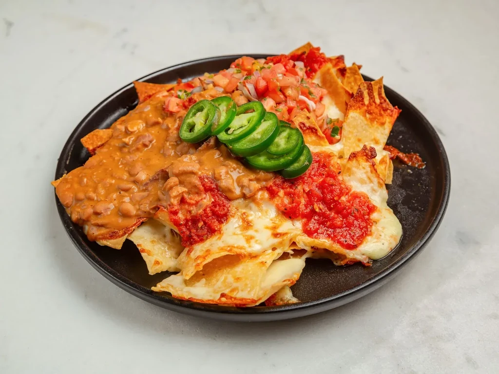 Nachos with beans, melted cheese, salsa, and jalapeños on a black plate.