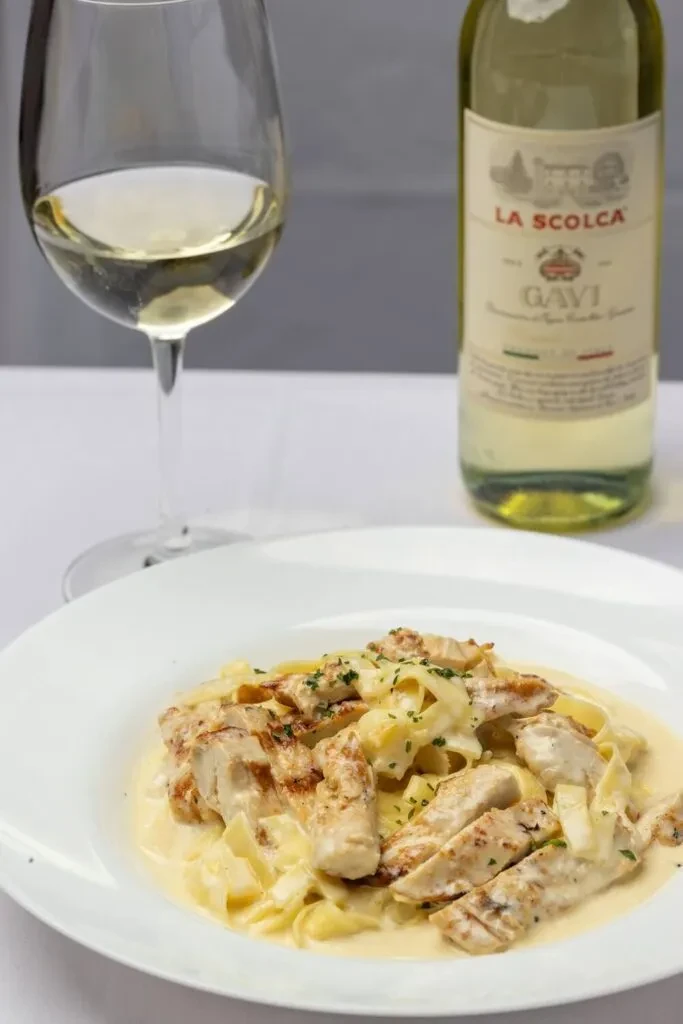 Fettuccine Alfredo with grilled chicken, white wine, and a wine bottle.