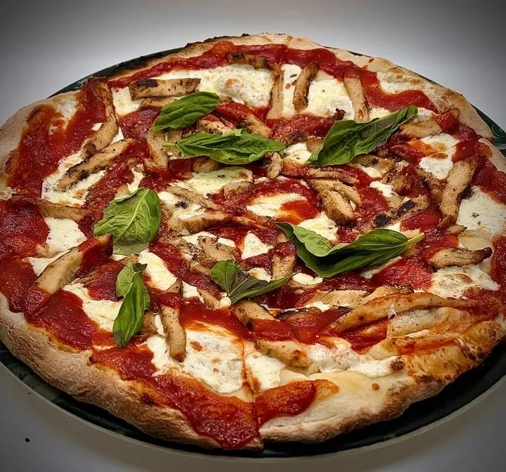 A whole pizza with chicken strips, tomato sauce, cheese, and basil.