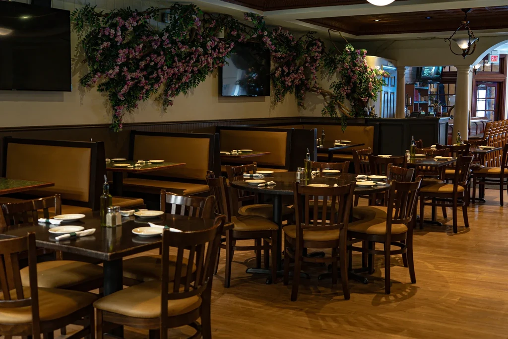 Empty dining room with tables and booths, decorated with artificial flowers.