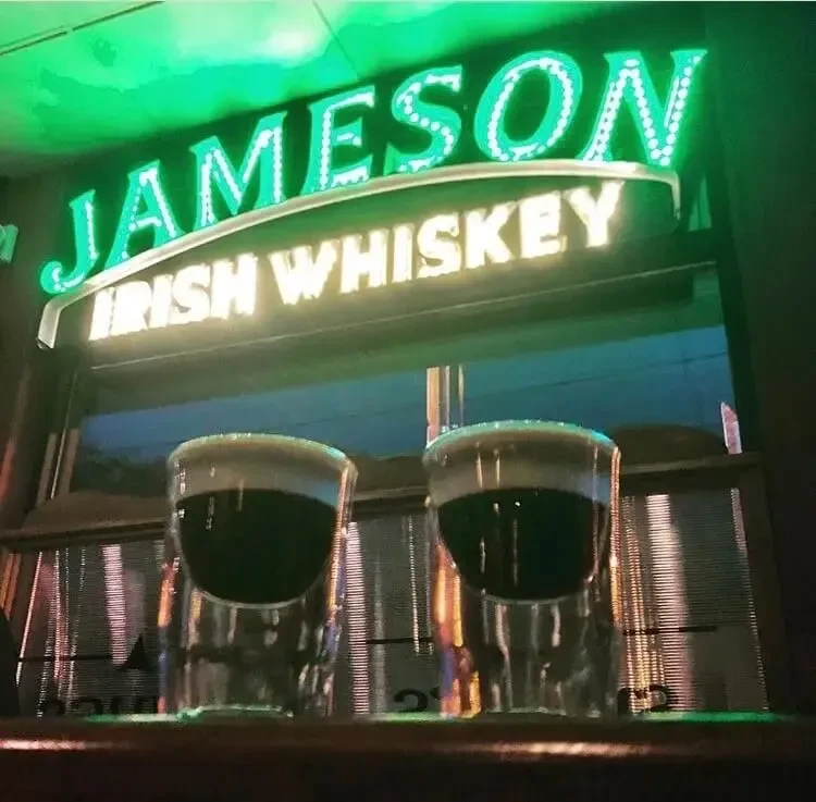 Two dark green shots with cream tops in front of a Jameson sign.