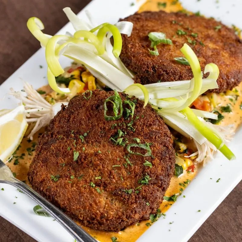 Two fried crab cakes with garnish on a bed of sauce.