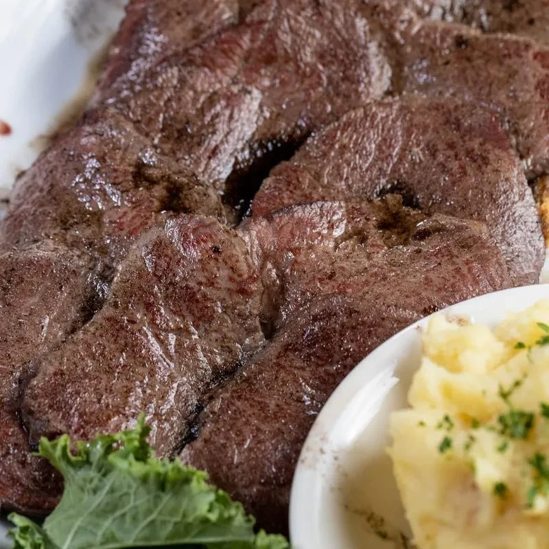 Seared beef liver, mashed potatoes, and kale on a white plate.