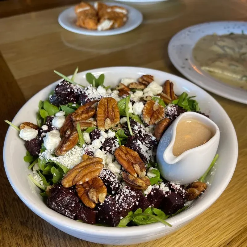 A white bowl of beet and pecan salad with a side of dressing.