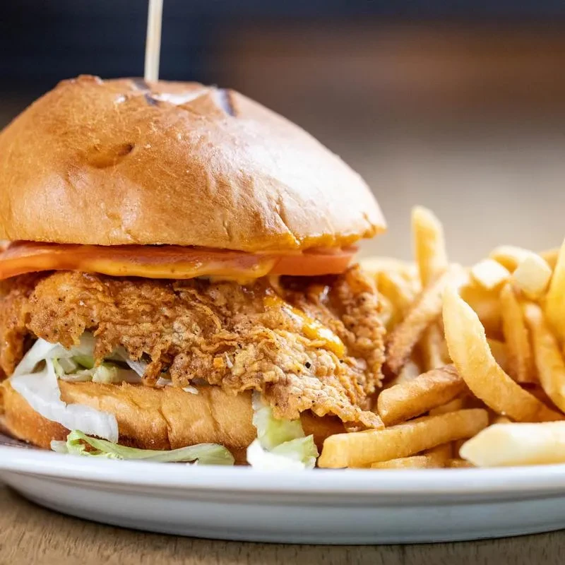 Fried chicken sandwich with lettuce, tomato, and a side of fries.