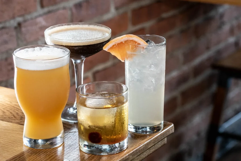 Four alcoholic drinks on a wooden bar in front of a brick wall.