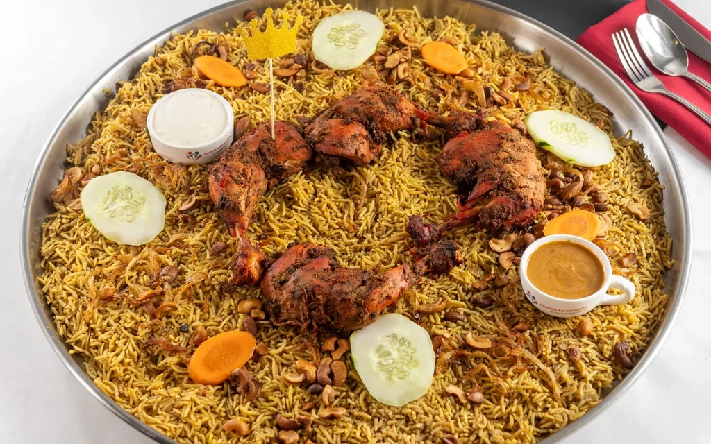 Large platter of mandi rice with roasted chicken, cucumber, and sauces.