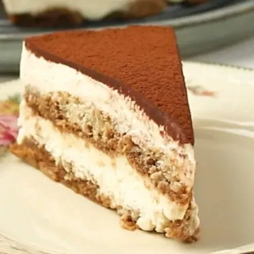 A slice of tiramisu cake with chocolate topping on a white plate.