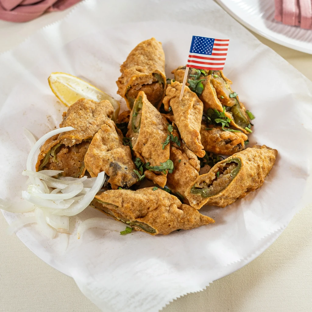 Fried green chiles with a lemon wedge and onions on white paper.