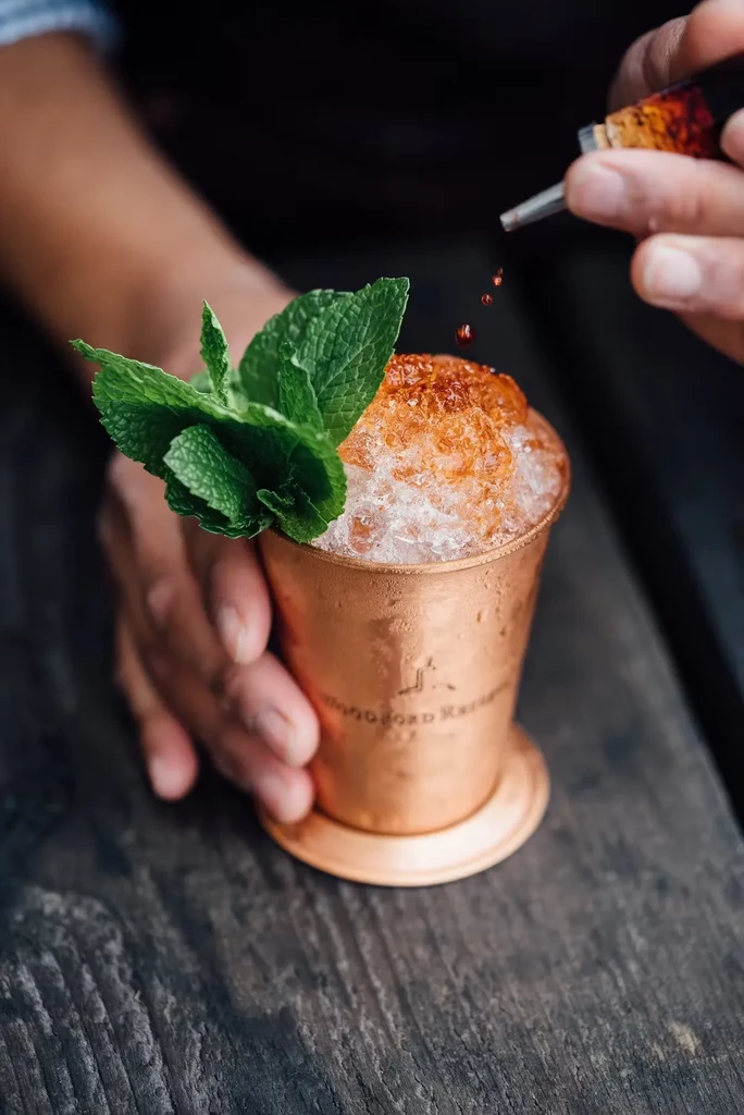 Someone adds drops of liquid to a copper mug with a cocktail.