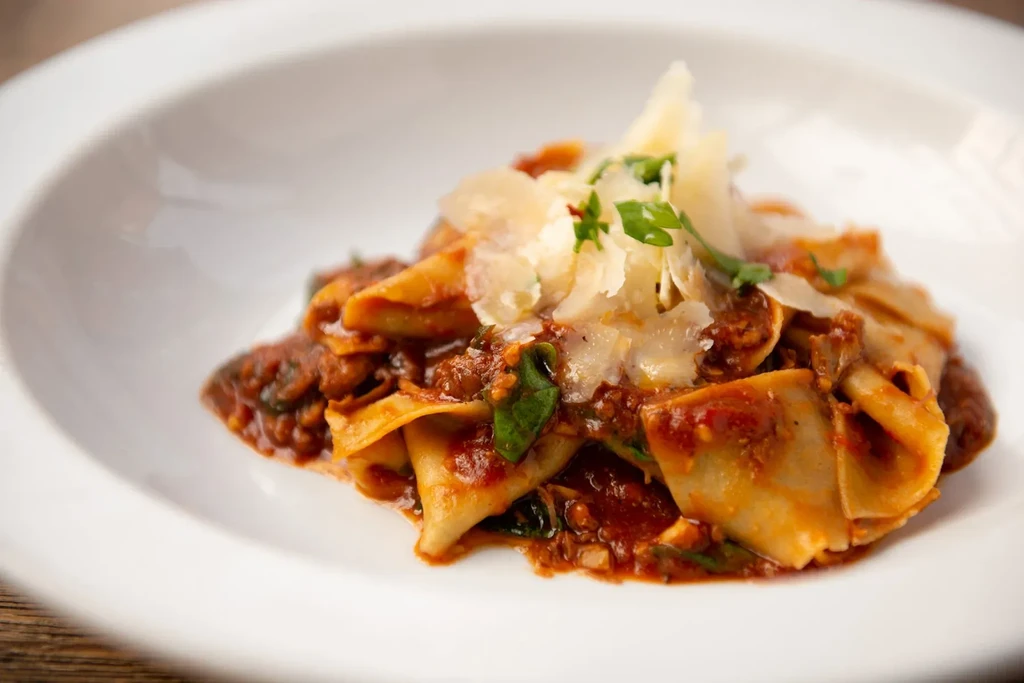 Pappardelle pasta with ragu sauce, topped with shaved parmesan cheese and parsley.