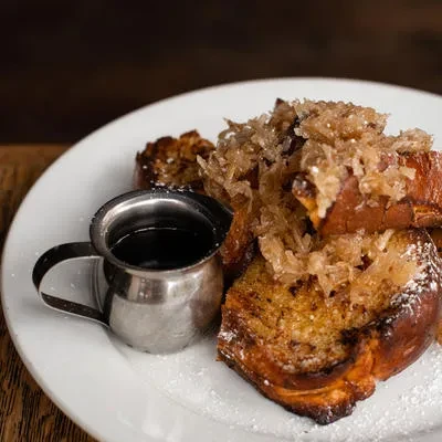 French toast with candied coconut and maple syrup on a white plate.