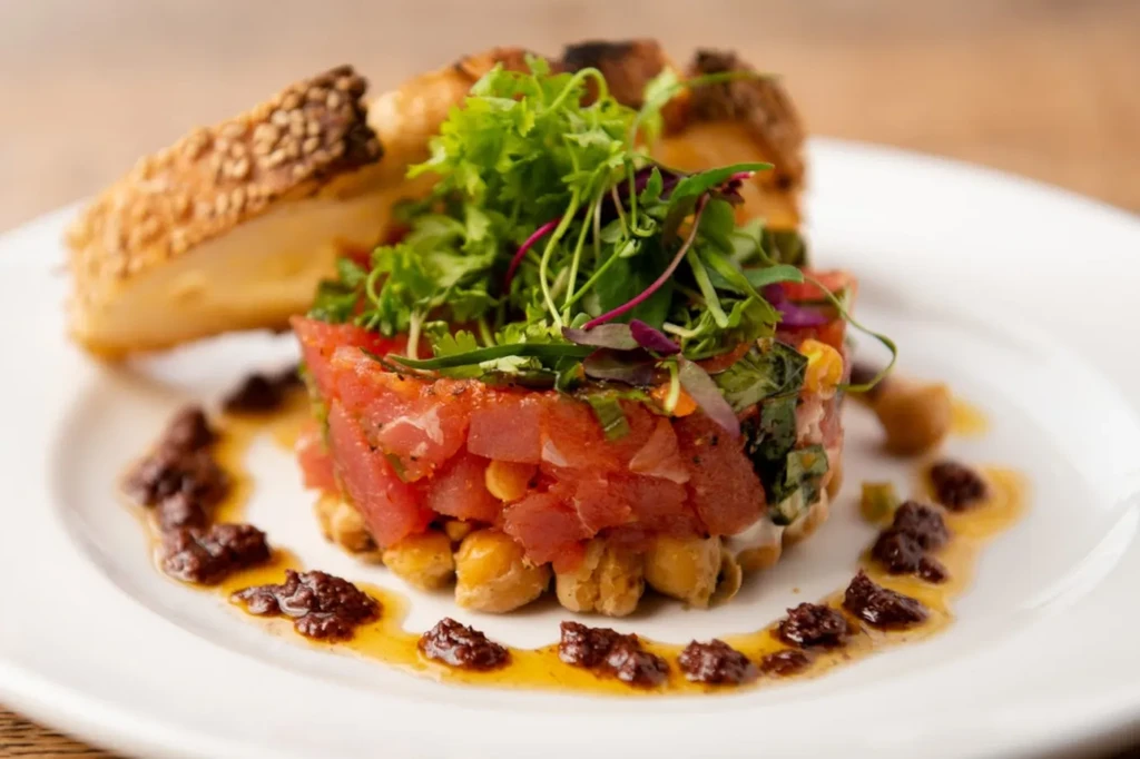Tuna tartare with greens and sesame bread on a white plate.