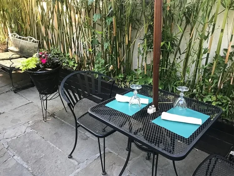 Outdoor patio with dining table set for two, bamboo plants.