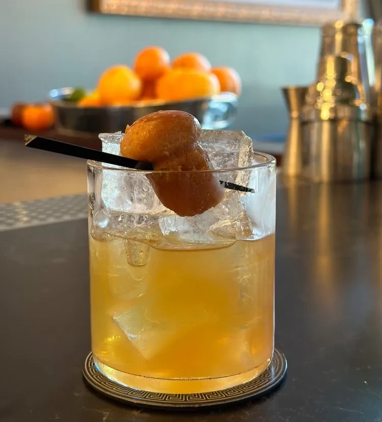 A cocktail with ice and a pastry on a skewer.