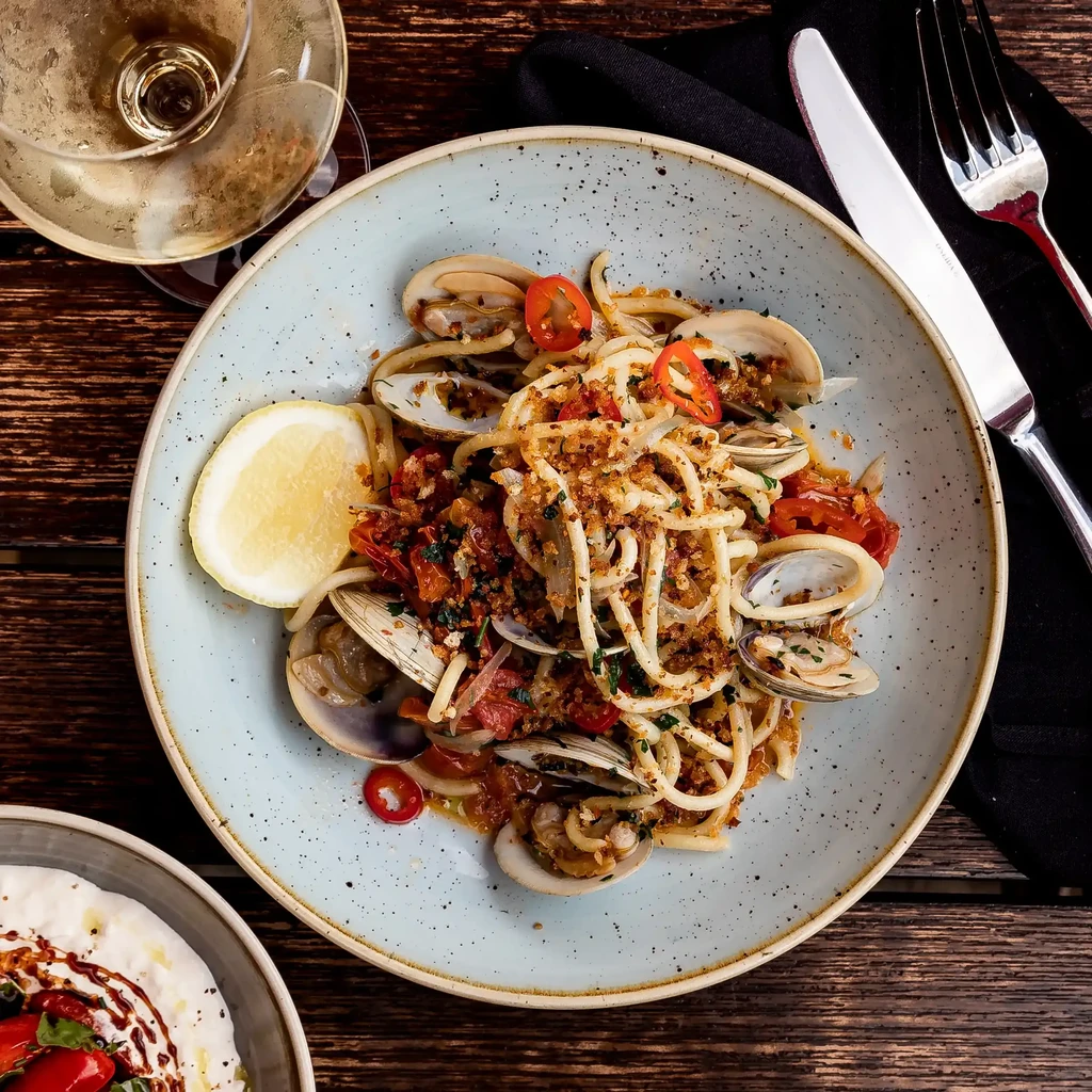 A plate of spaghetti with clams, cherry tomatoes, and red chili.