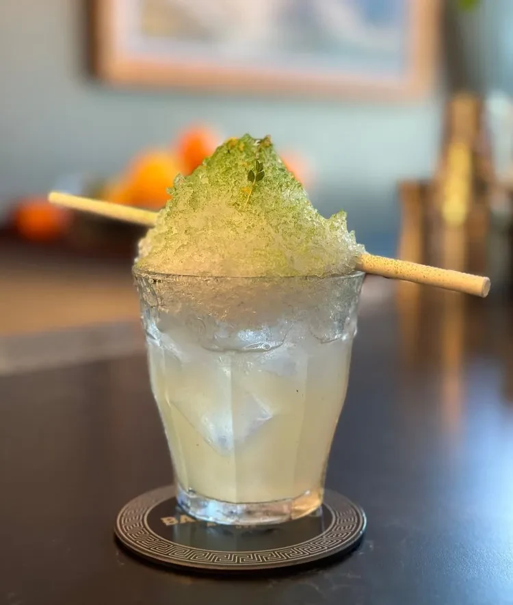 Cocktail in glass with green-dusted crushed ice and a straw.