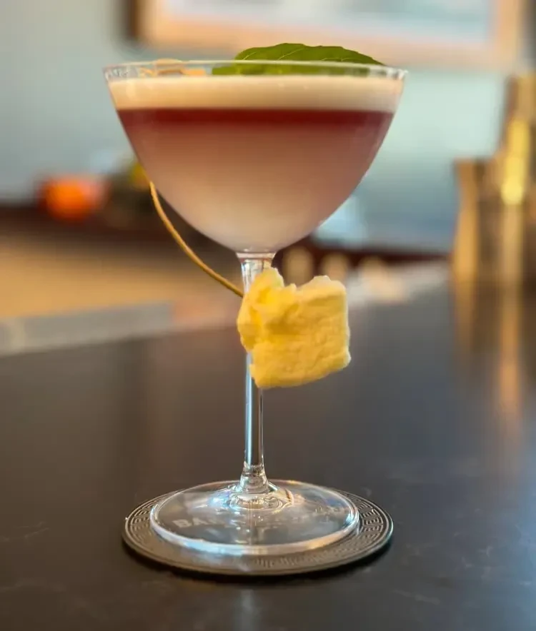 A pink cocktail in a coupe glass garnished with a mint leaf.