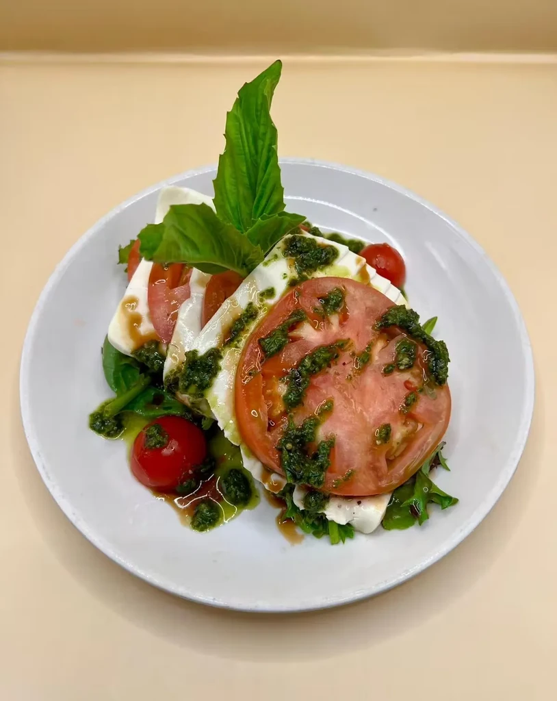 Caprese salad with sliced tomatoes, mozzarella, pesto, and basil.