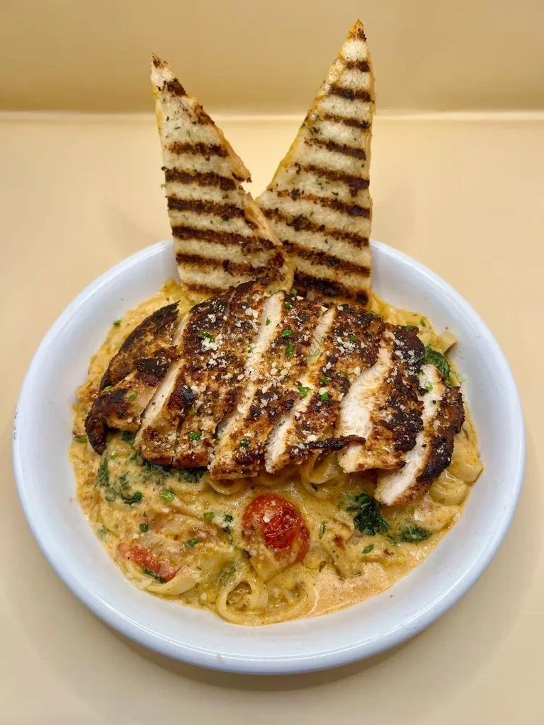 Creamy pasta with sliced grilled chicken, spinach, tomatoes, and grilled bread.