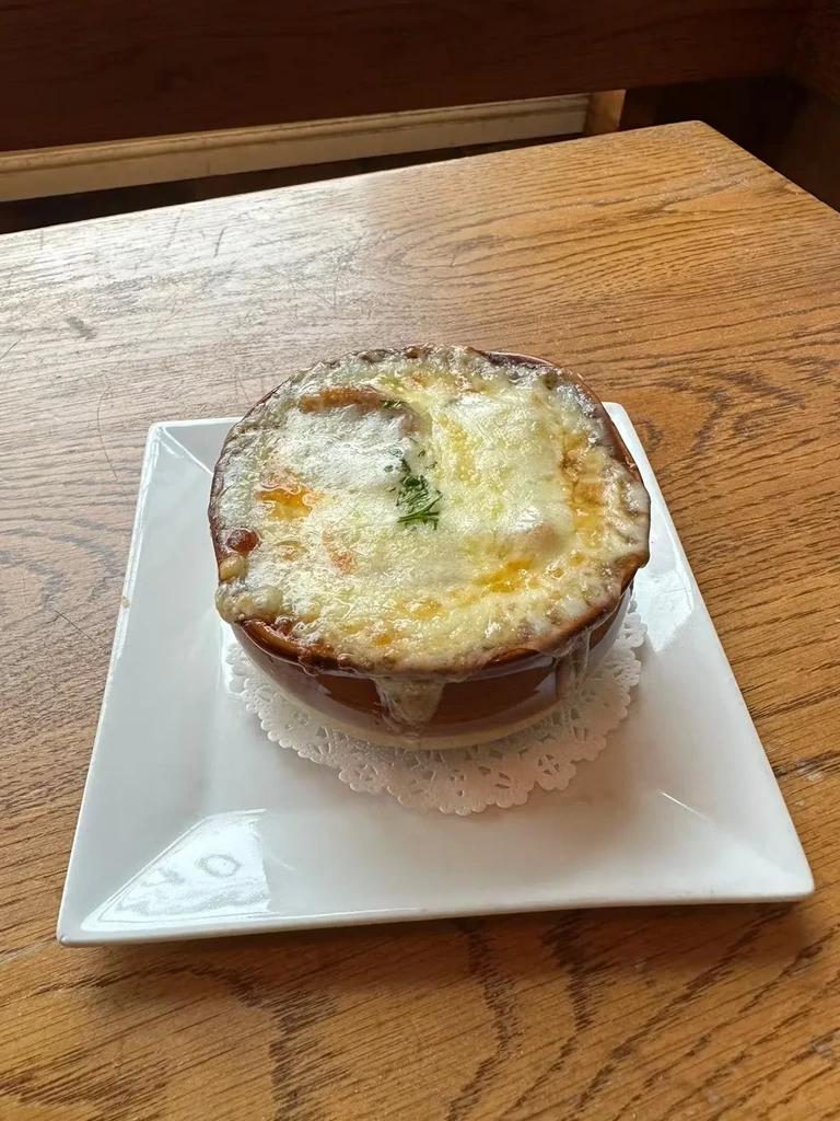 A crock of French onion soup with melted cheese on a wooden table.