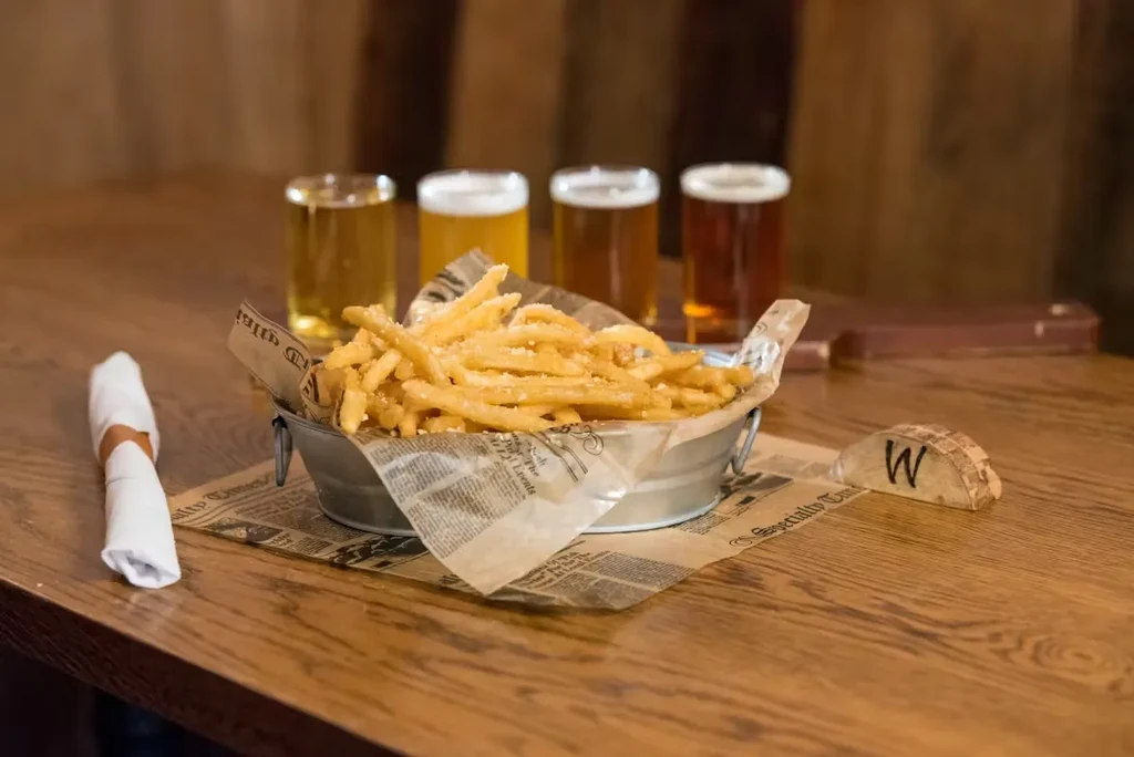 Fries in a metal bucket and four beers on a wooden table.