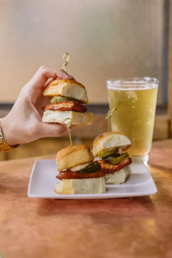Hand holding a chicken slider with pickles and a glass of beer.