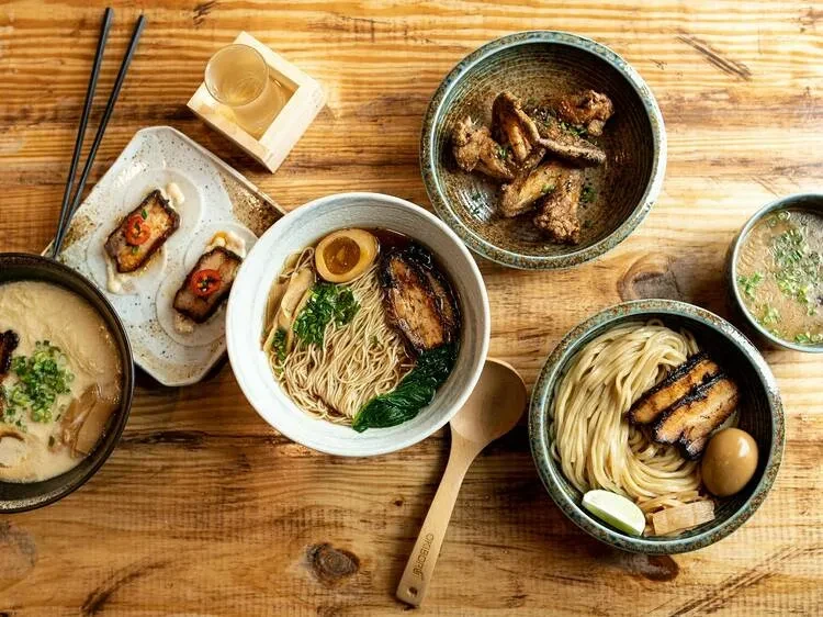 Assortment of ramen bowls, chicken wings, and sake on a wooden table.