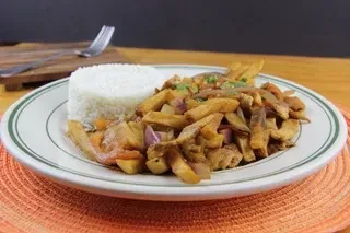 Peruvian lomo saltado with white rice on a white and green plate.