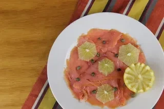 Smoked salmon carpaccio with lemon, capers, and a striped napkin on wood.