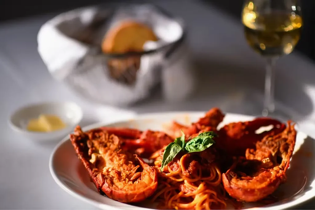 A plate of lobster pasta with basil, bread, and wine.