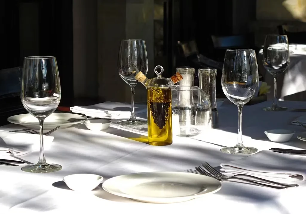 A restaurant table set with wine glasses, plates, and an olive oil dispenser.