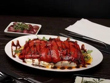 Roasted red peppers with mozzarella, drizzled with balsamic glaze, on a white plate.