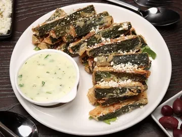 Fried zucchini sticks with feta cheese and a side of dipping sauce.