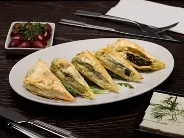 Five spinach-filled pastry triangles on a white platter, with olives and feta.